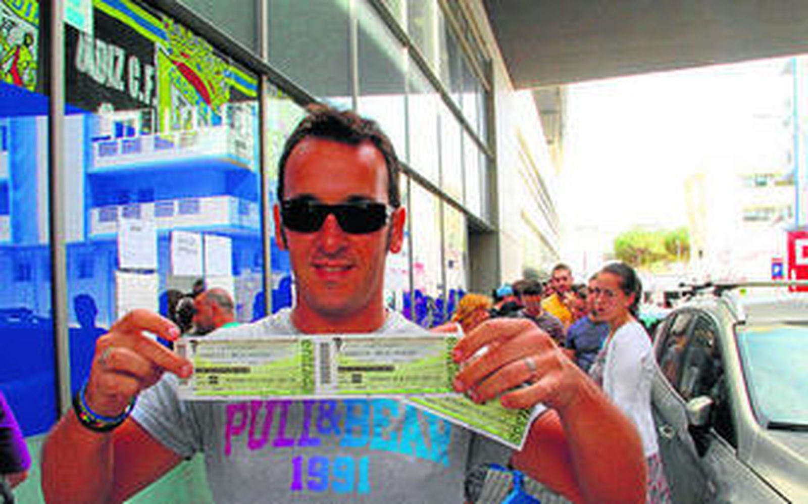 Un aficionado amarillo muestra las entradas adquiridas ayer, con una cola trás él.