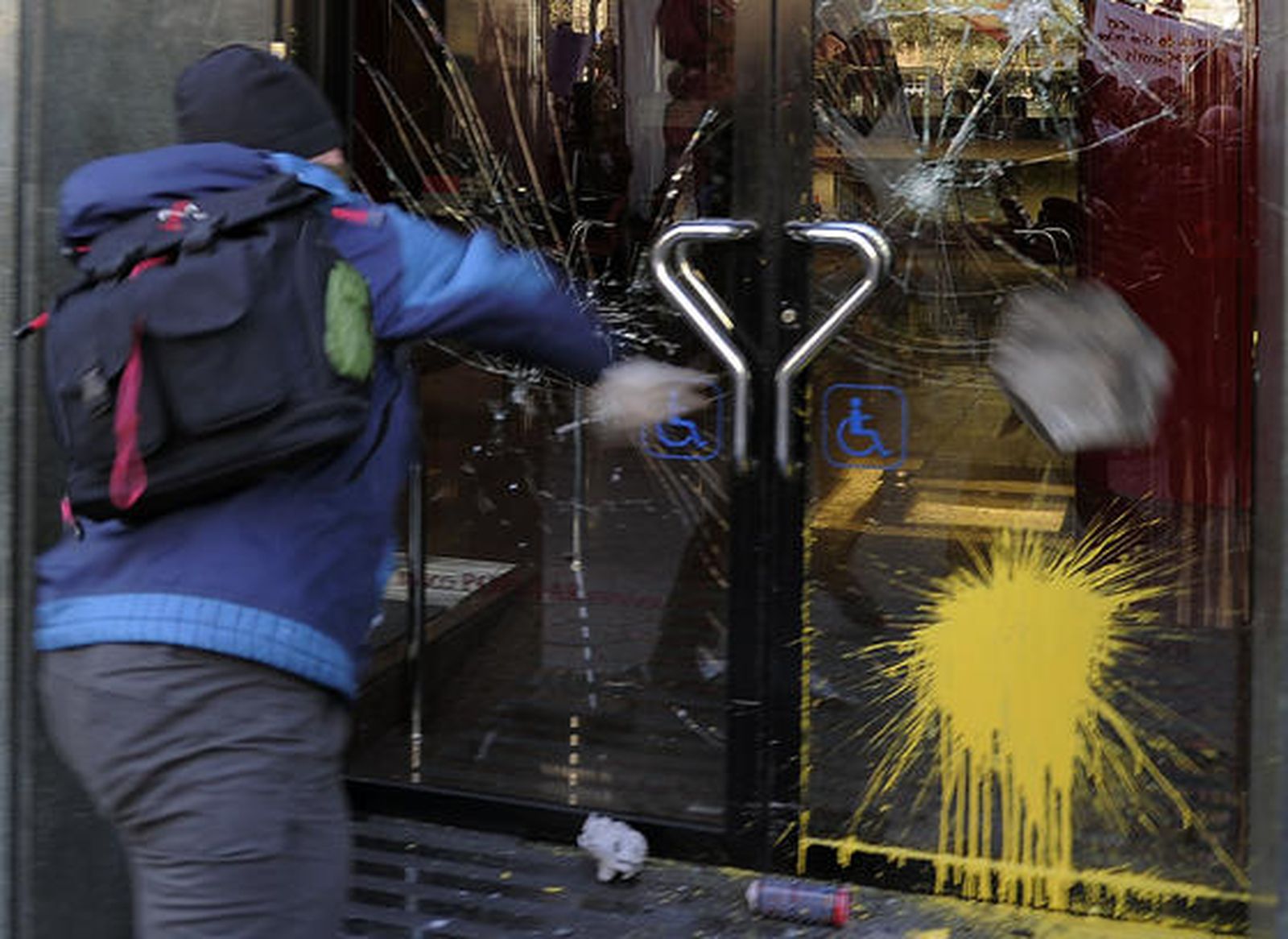 Un joven lanza piedras y bolas de pintura contra un banco.  Foto: Afp