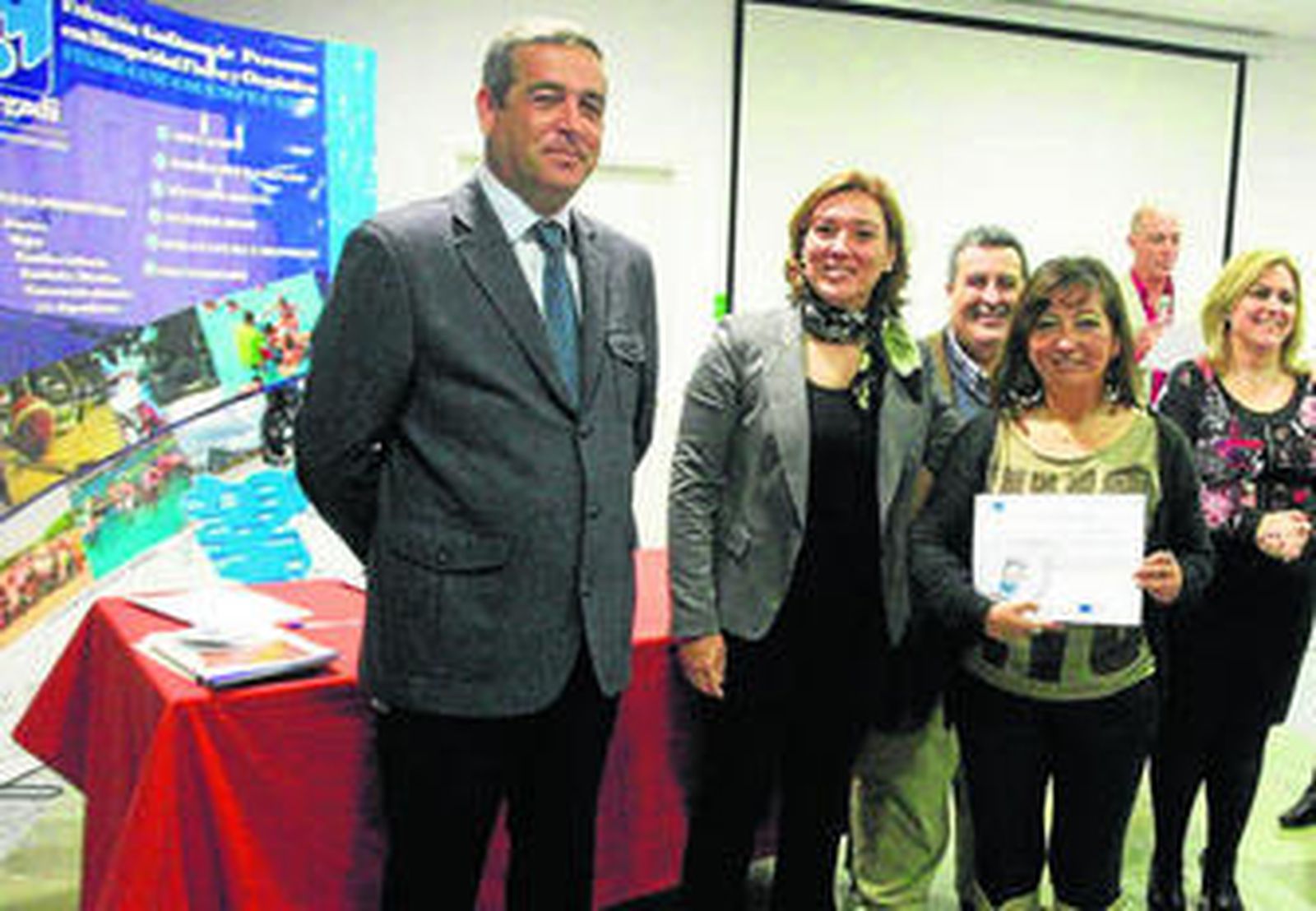 Una de las alumnas recoge su título, junto a la alcalesa y otros responsables políticos.