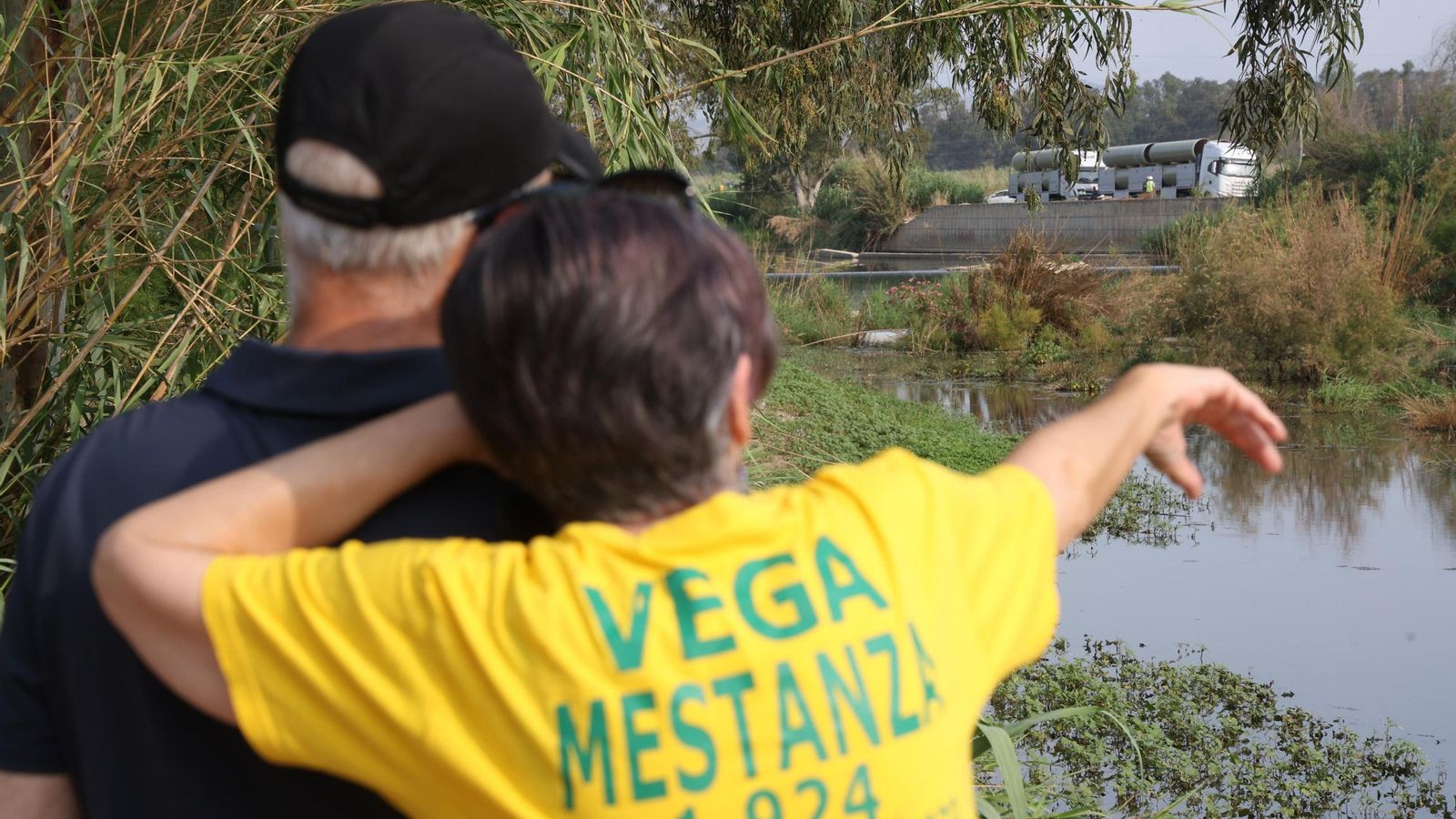 Dos asistentes a la concentración, junto al río, señalan unos camiones con material estacionados en la zona.