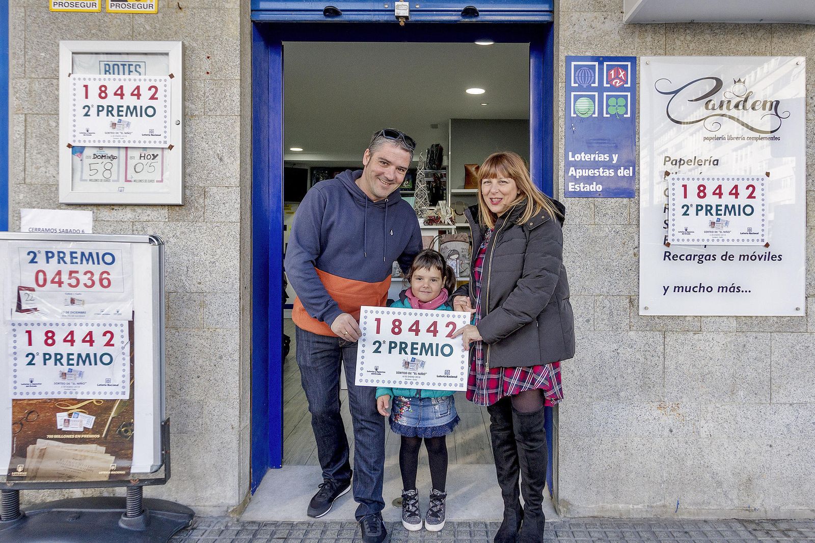 Juan Antonio y Marián posan con el cartel del número premiado en la puerta de la papelería Candem.