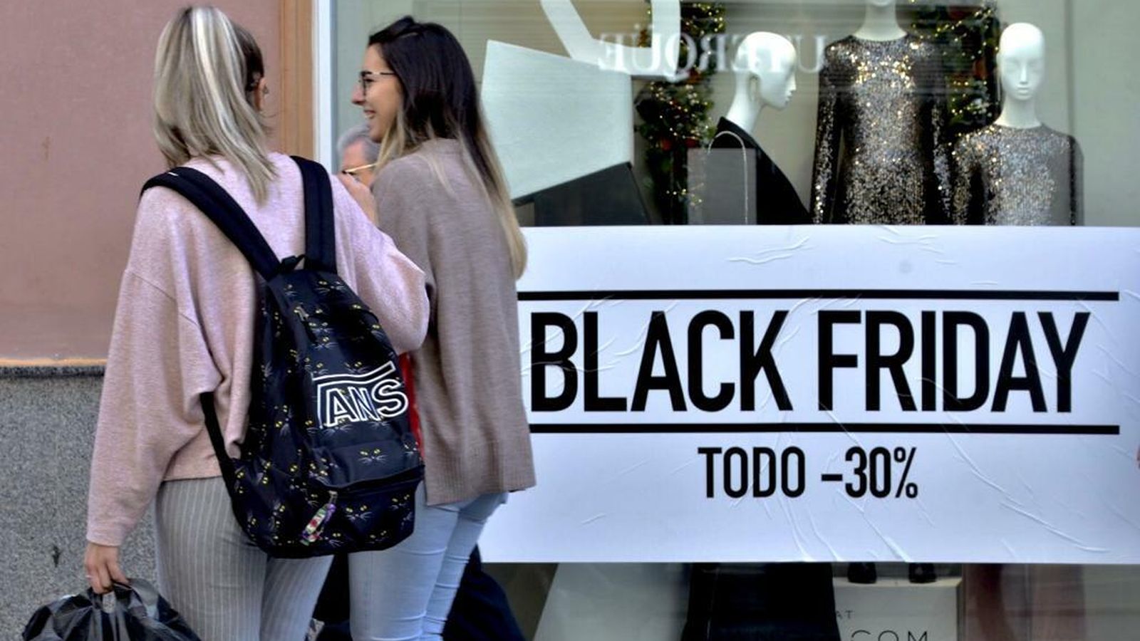 Dos jóvenes pasean por el centro al lado de una tienda con importantes descuentos.