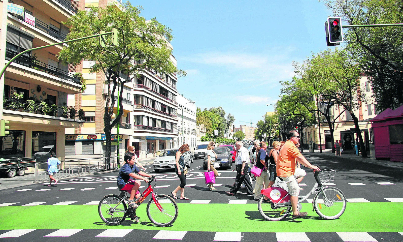 Peatones y ciclistas pasan por la ronda histórica de Sevilla mientras los coches esperan en el semáforo.