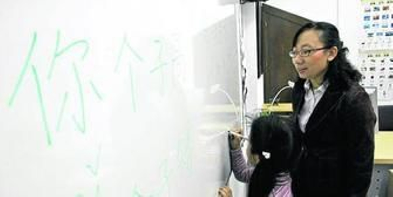 Una niña escribe los caracteres chinos en una pizarra ante la mirada de su profesora.