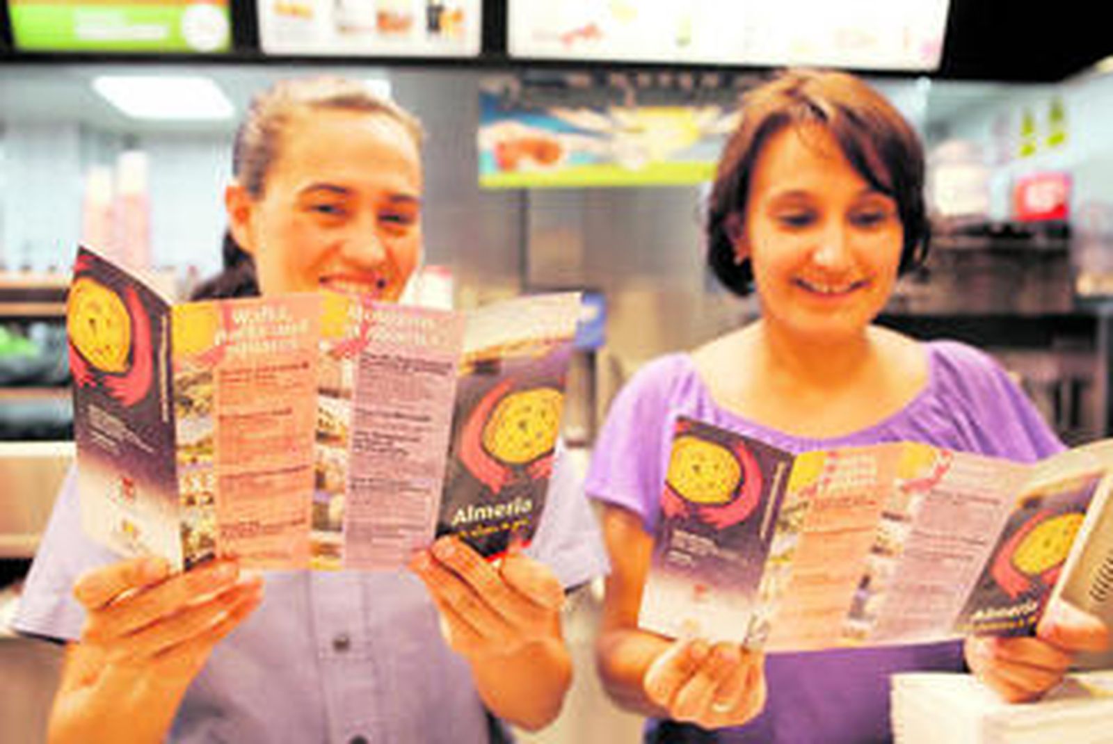 Los folletos turísticos, que sujetan dos dependientas del McDonald's, están editados en inglés y español.