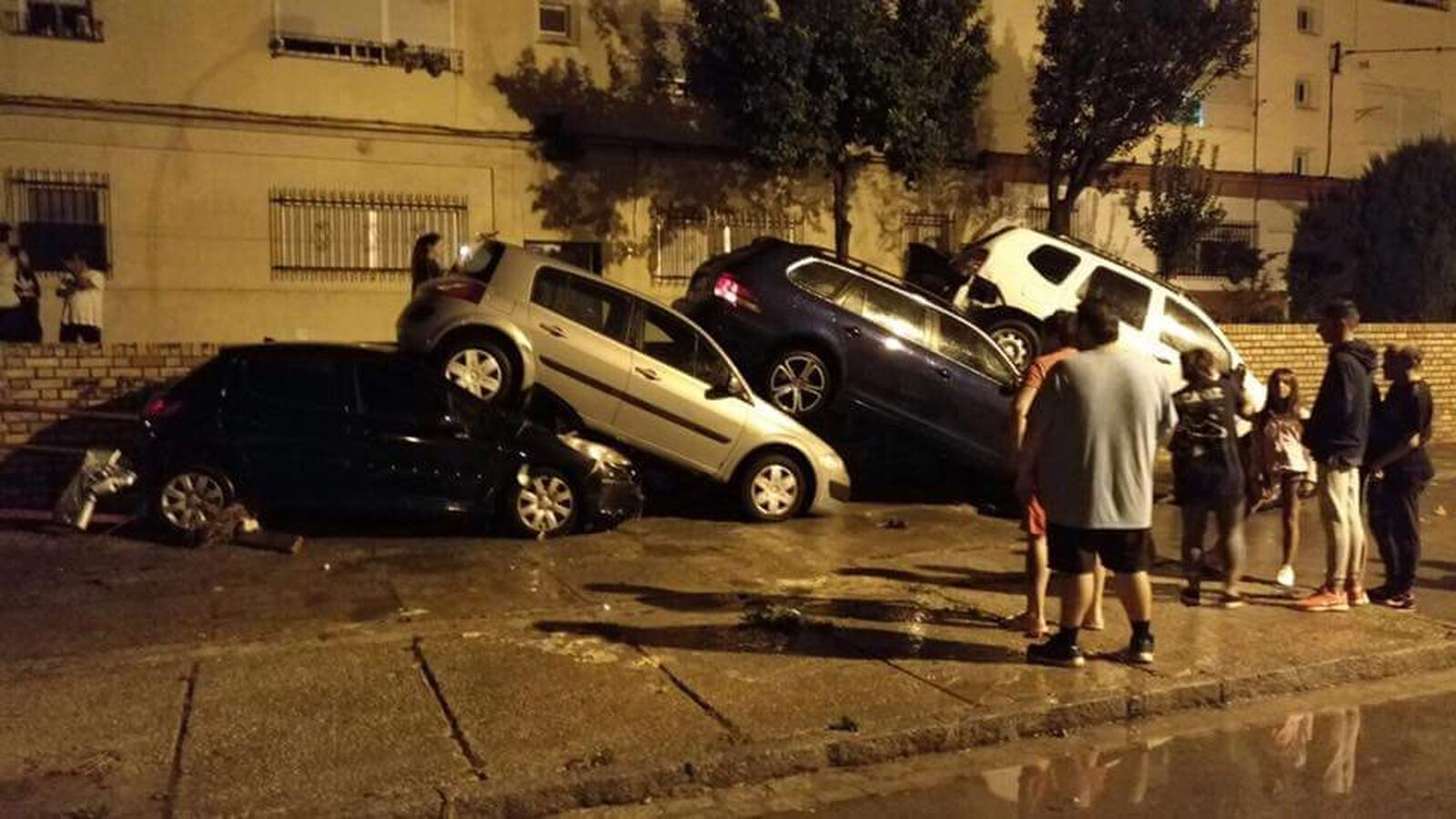 Vecinos de la calle Porvera observan con asombro hasta cuatro vehículos montados unos encima de otros a causa de la riada.