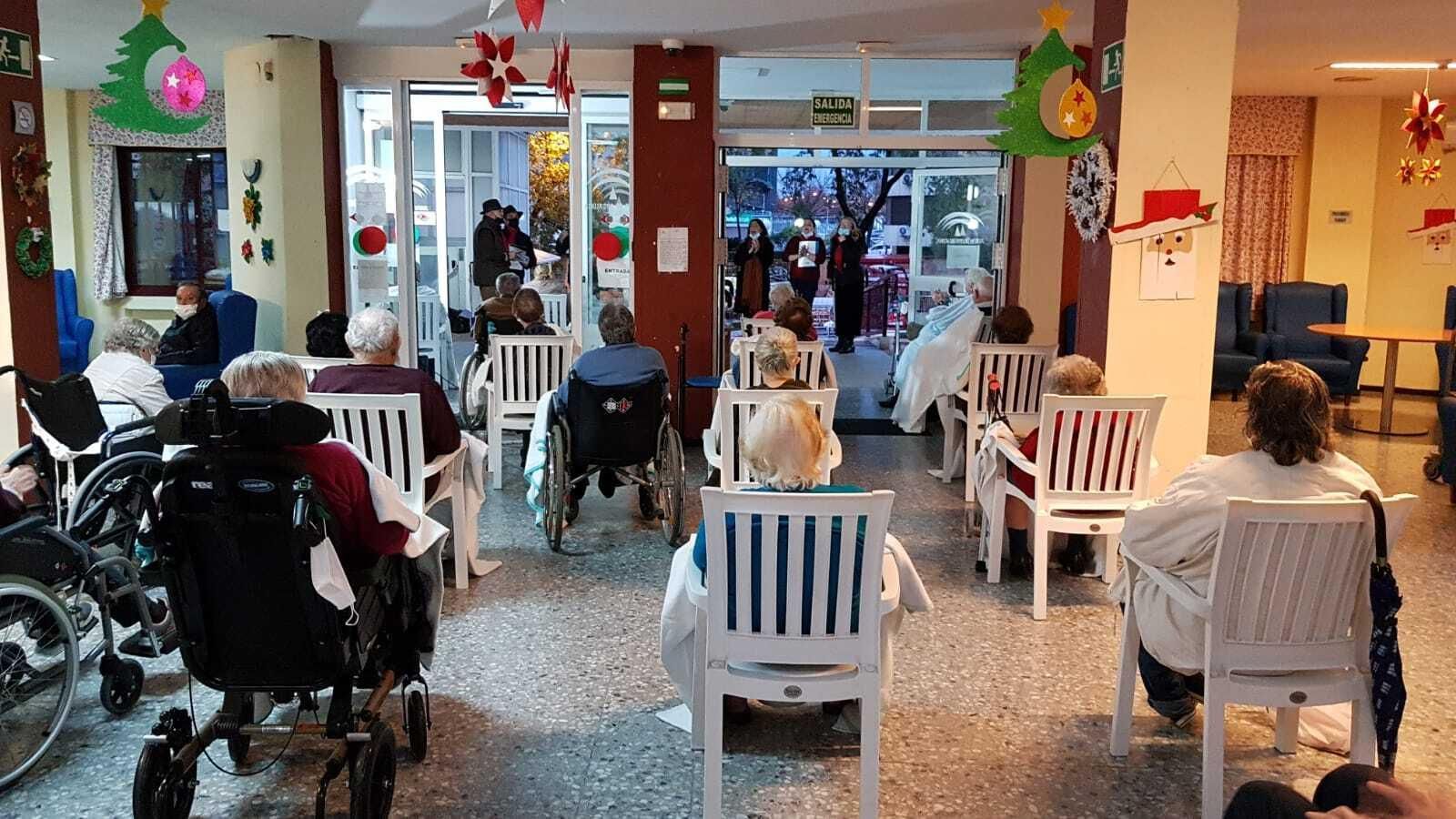 Los usuarios de la residencia Heliópolis, disfrutan de la actuación de un coro de Navidad, desde fuera del centro.