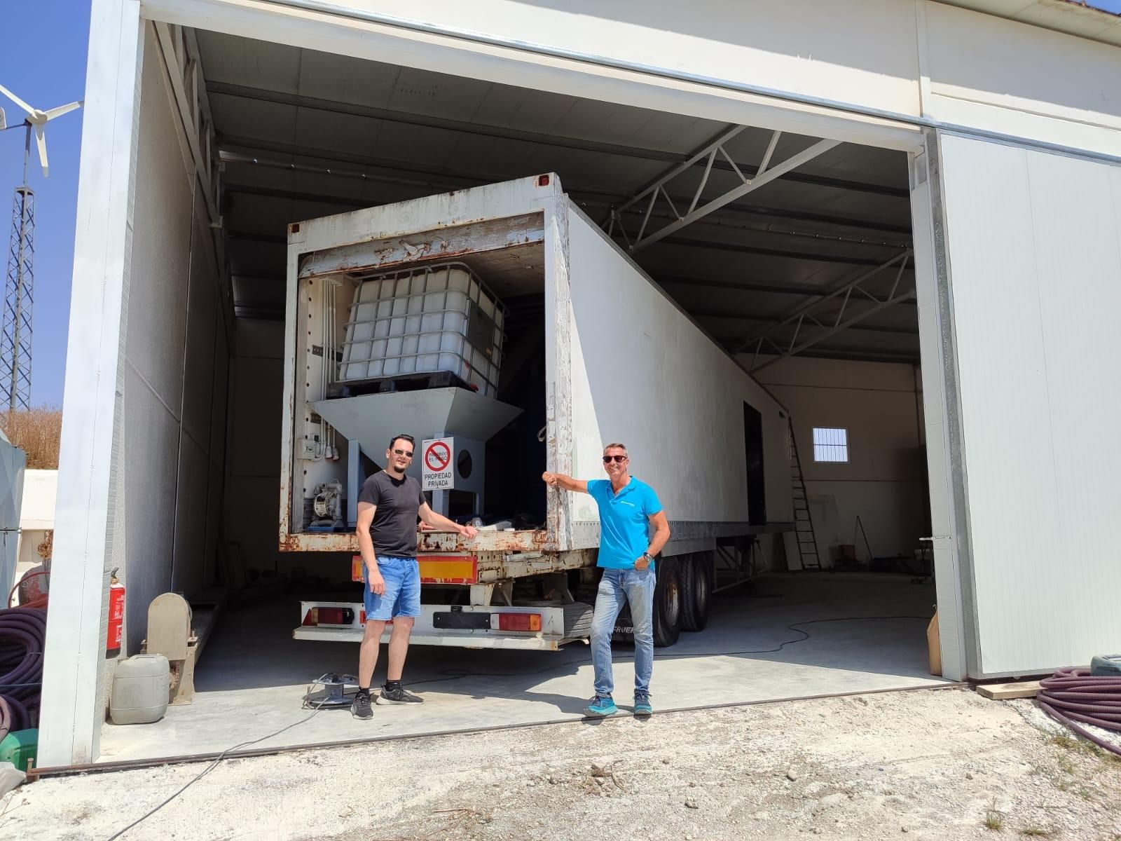 Daniel Téllez y Domingo Pérez junto a la almazara portátil instalada en el interior del tráiler en la finca de Torrecera