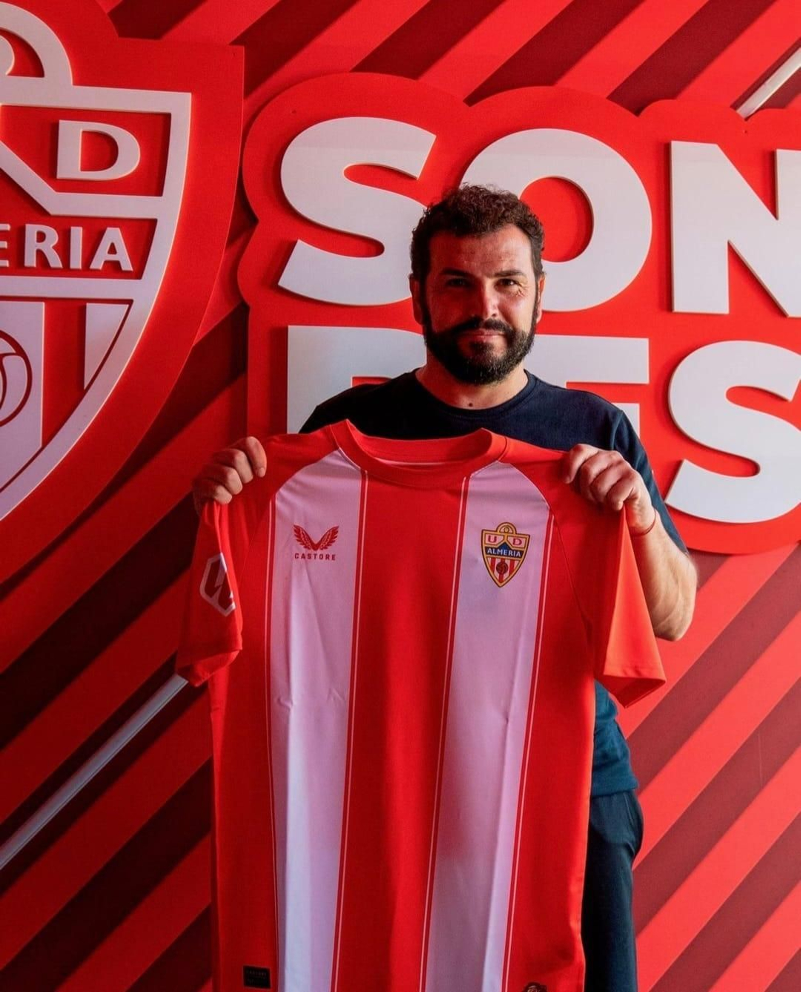 El nuevo técnico del conjunto almeriense posa con la camiseta de los rojiblancos en el túnel de vestuarios del Estadio de los Juegos Mediterráneos.