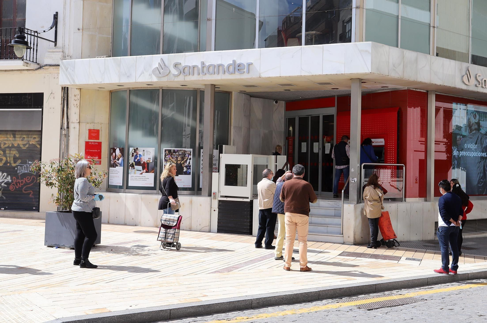 Varias personas guardan cola fuera de una entidad bancaria.