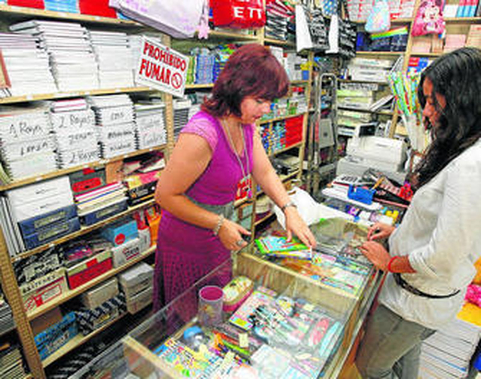 Una dependienta, vendiendo material escolar en un pequeño comercio.