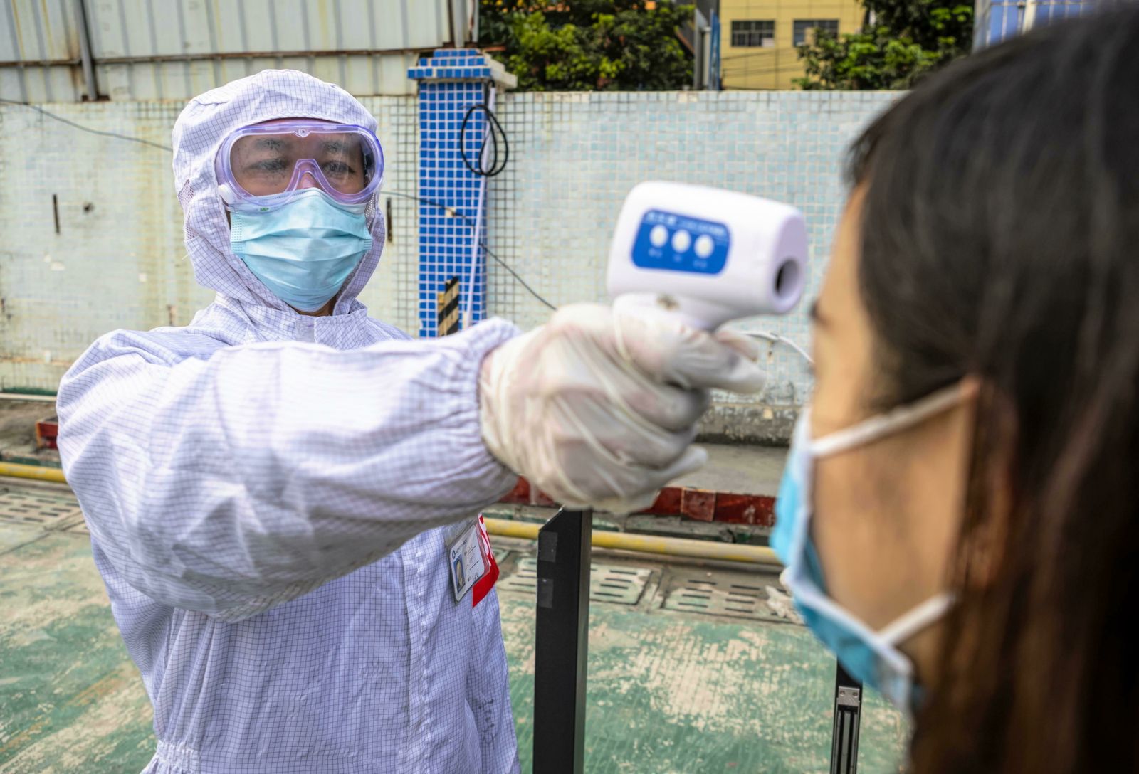 Personal de seguridad toma la temperatura a una empleada en una fábrica china.