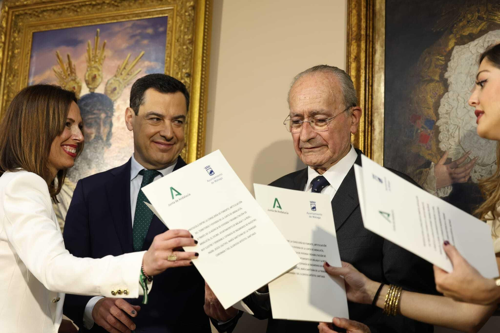 En el centro, Juanma Moreno, presidente de la Junta de Andalucía, y Francisco de la Torre, alcalde de Málaga, intercambian los documentos para la cesión.
