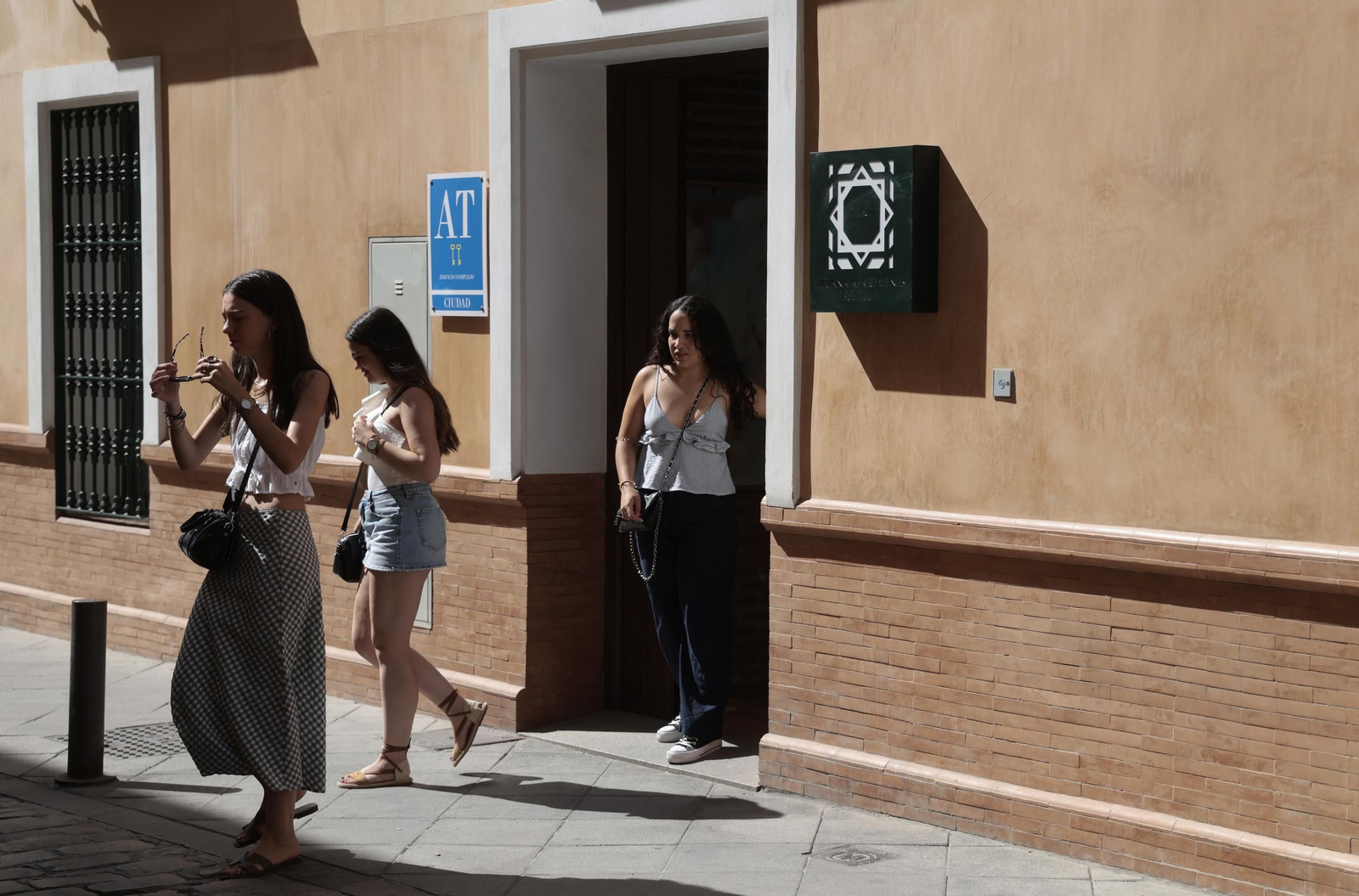 Tres turistas salen de unos apartamentos turísticos en la calle Alfarería.