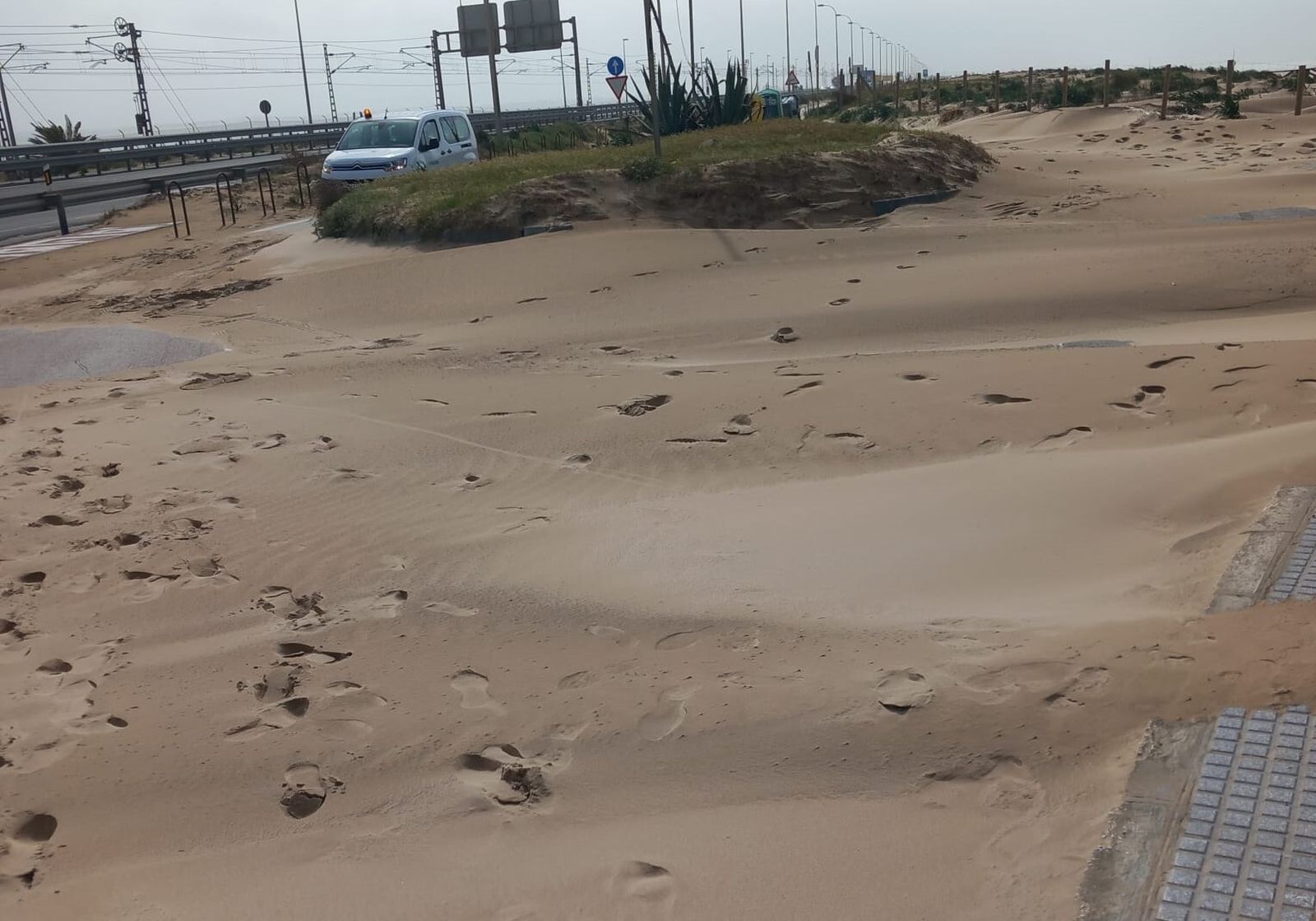 La vía de servicio de la playa de Cortadura cubierta por la arena
