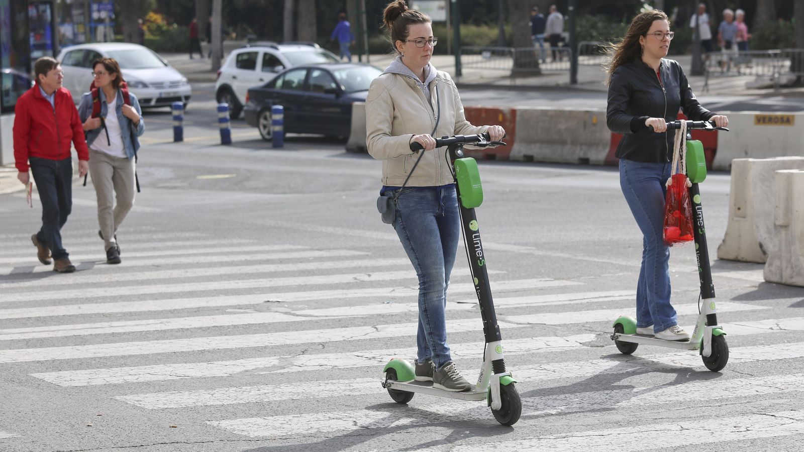 Dos usuarias atraviesan un paso de peatones sobre el patinete.