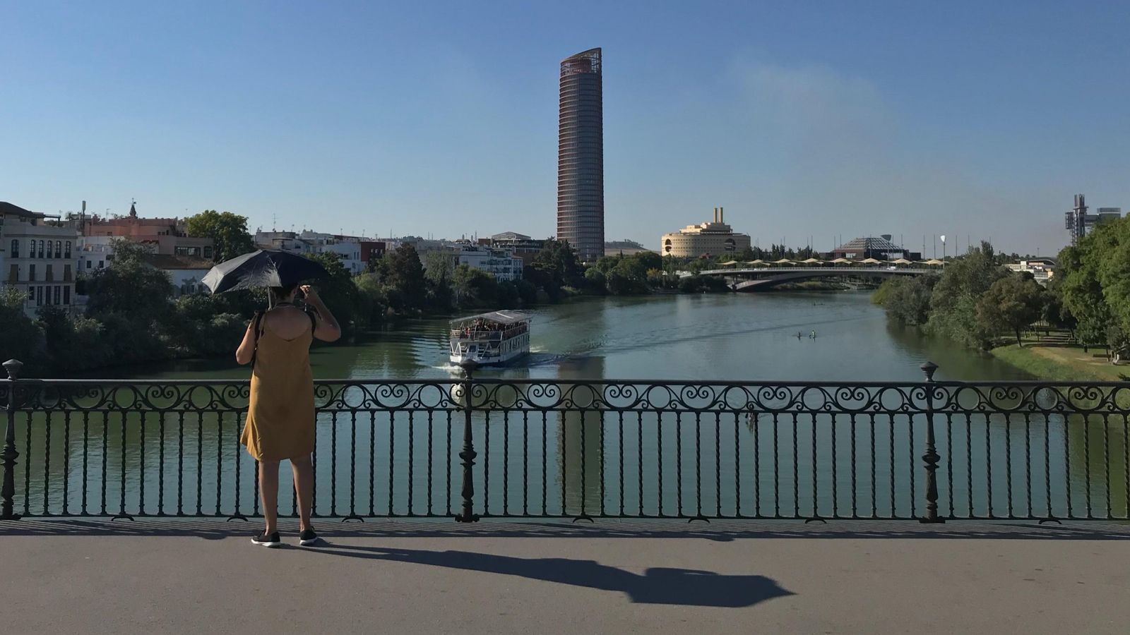 Una mujer se cubre del sol en el Puente de Triana, con la Torre Sevilla al fondo.