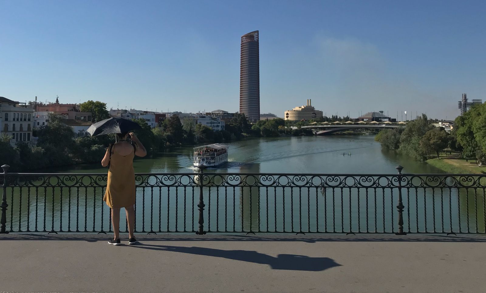 Una mujer se cubre del sol en el Puente de Triana, con la Torre Sevilla al fondo.