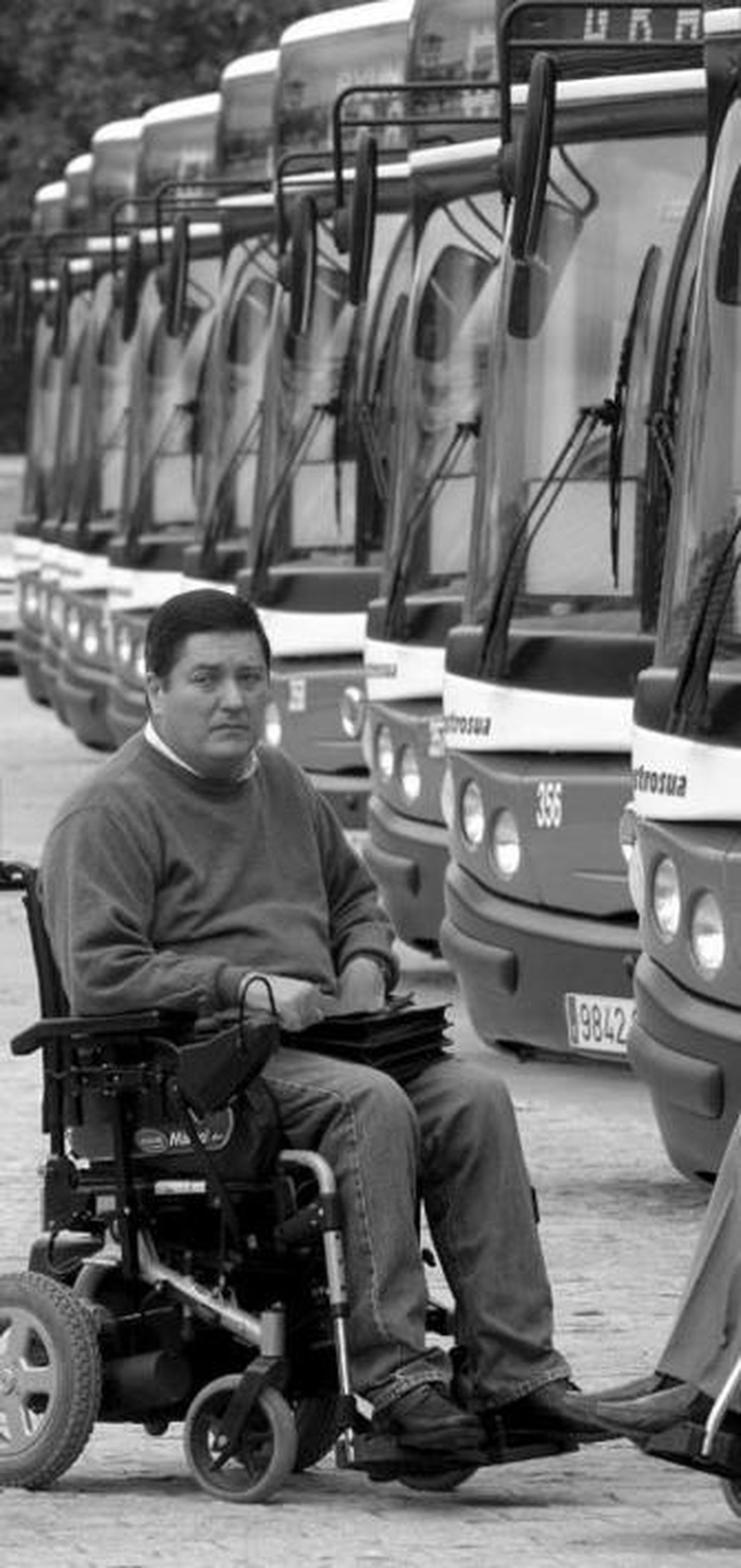 Un minusválido, junto a la flota de autobuses.