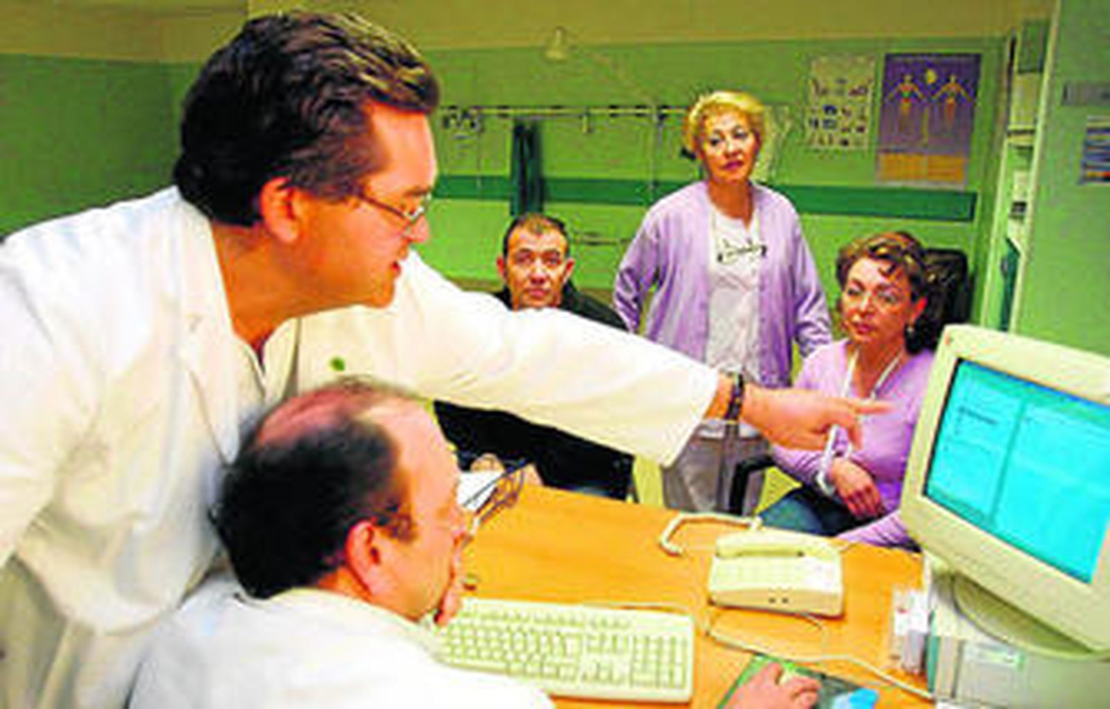 Dos facultativos consultan datos en el programa Diraya, ante unos pacientes.