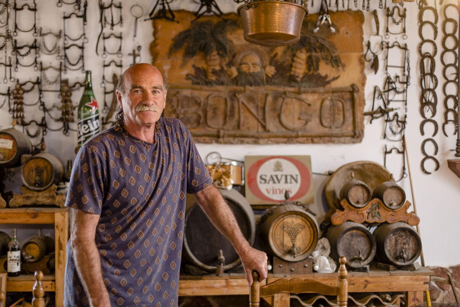 Carlos posa en su casa delante del cartel del pub de la segunda pista con el que inició su aventura hostelera más fructífera.