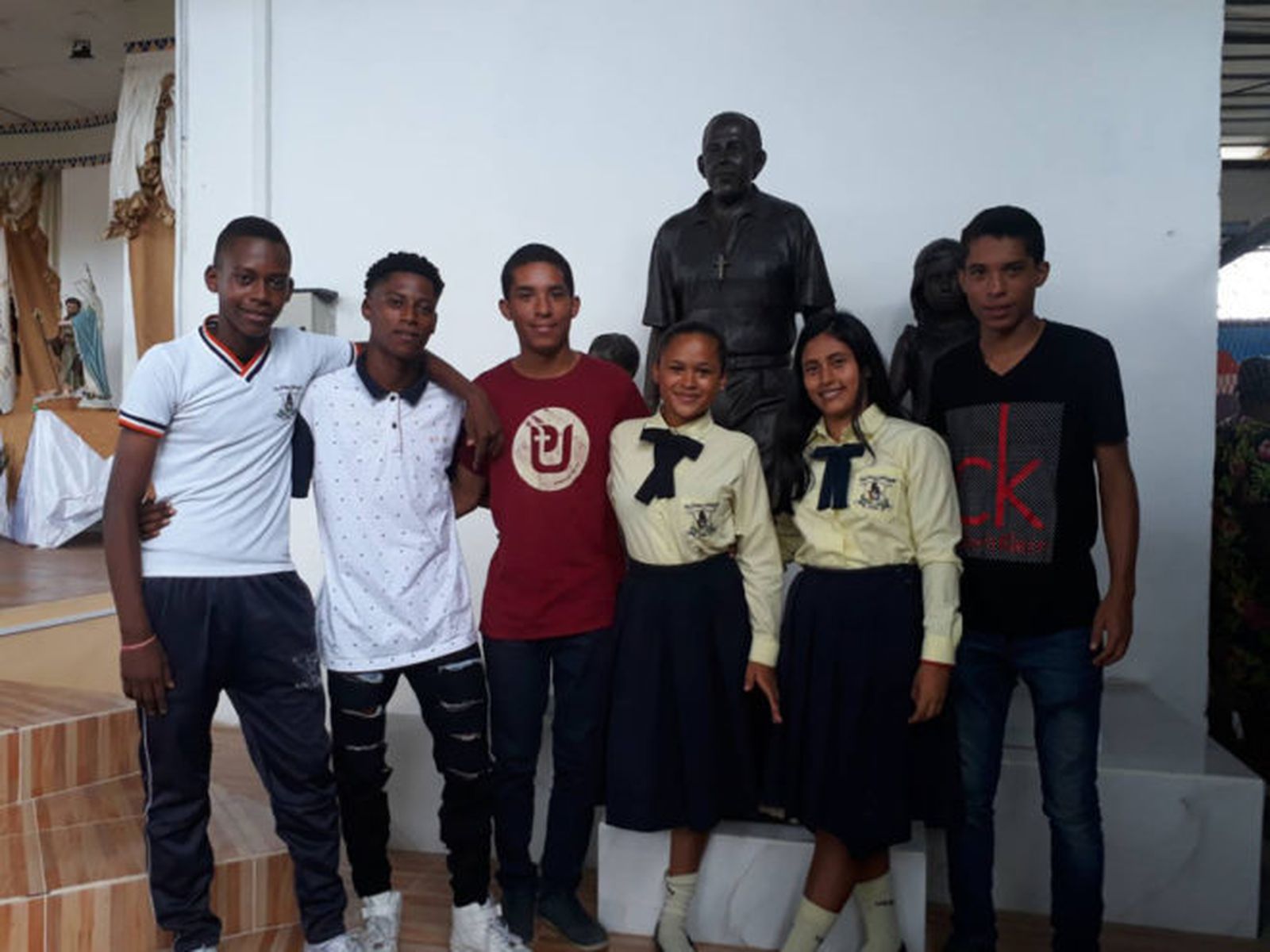 Seis de los siete jóvenes que salvó el religioso, junto a una réplica de la estatua.