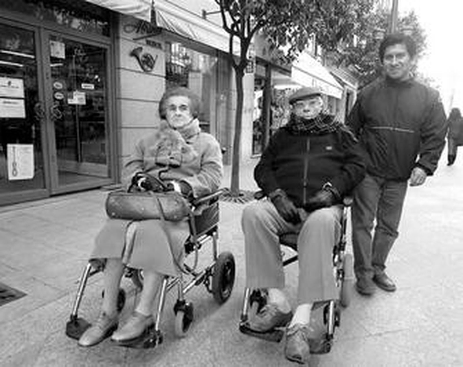 Dos personas mayores en silla de ruedas, por la calle Lancería.