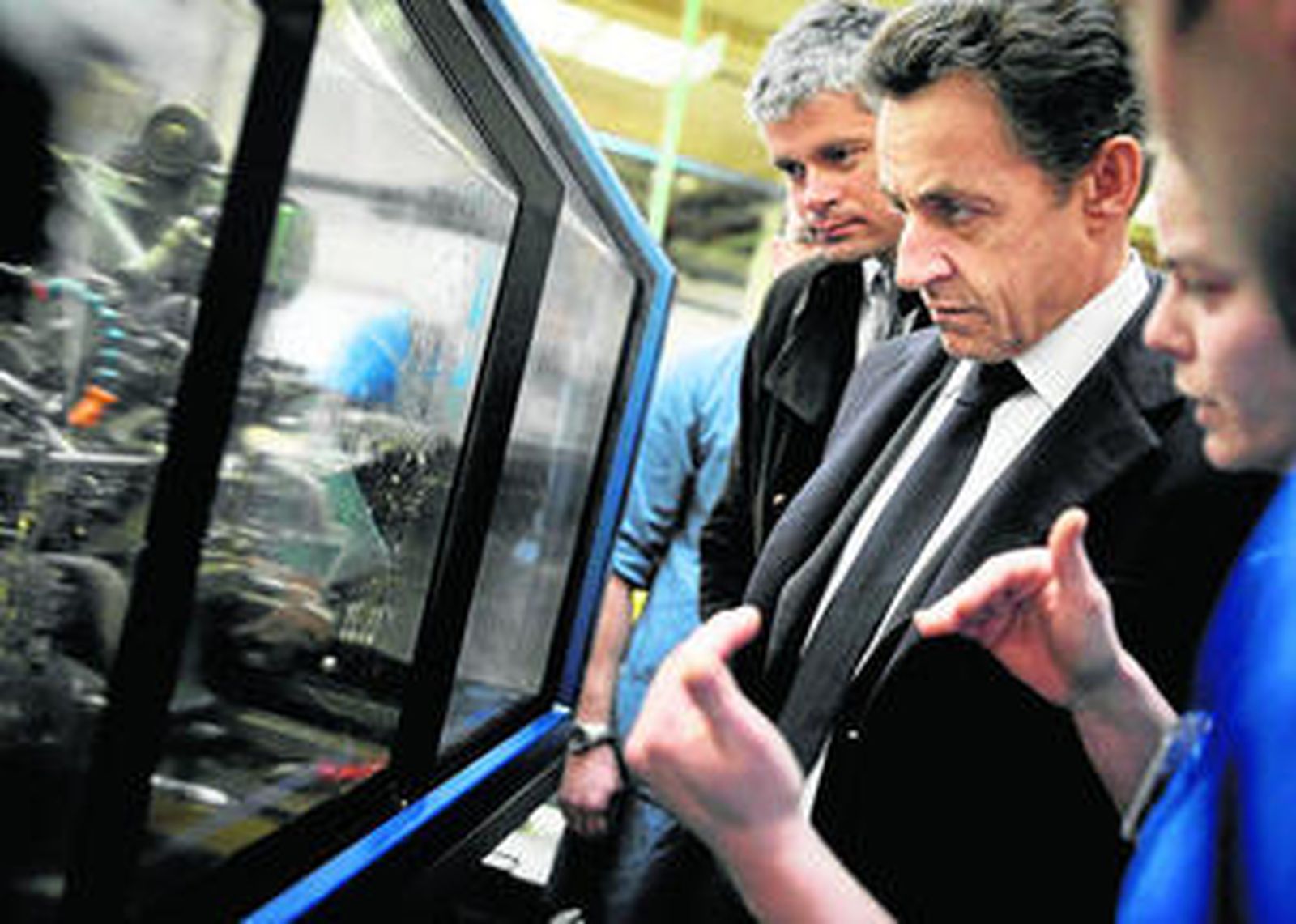 El presidente Nicolas Sarkozy, flanqueado por el ministro de Empleo, atiende a las explicaciones de los trabajadores de una fábrica en Pontarlier.