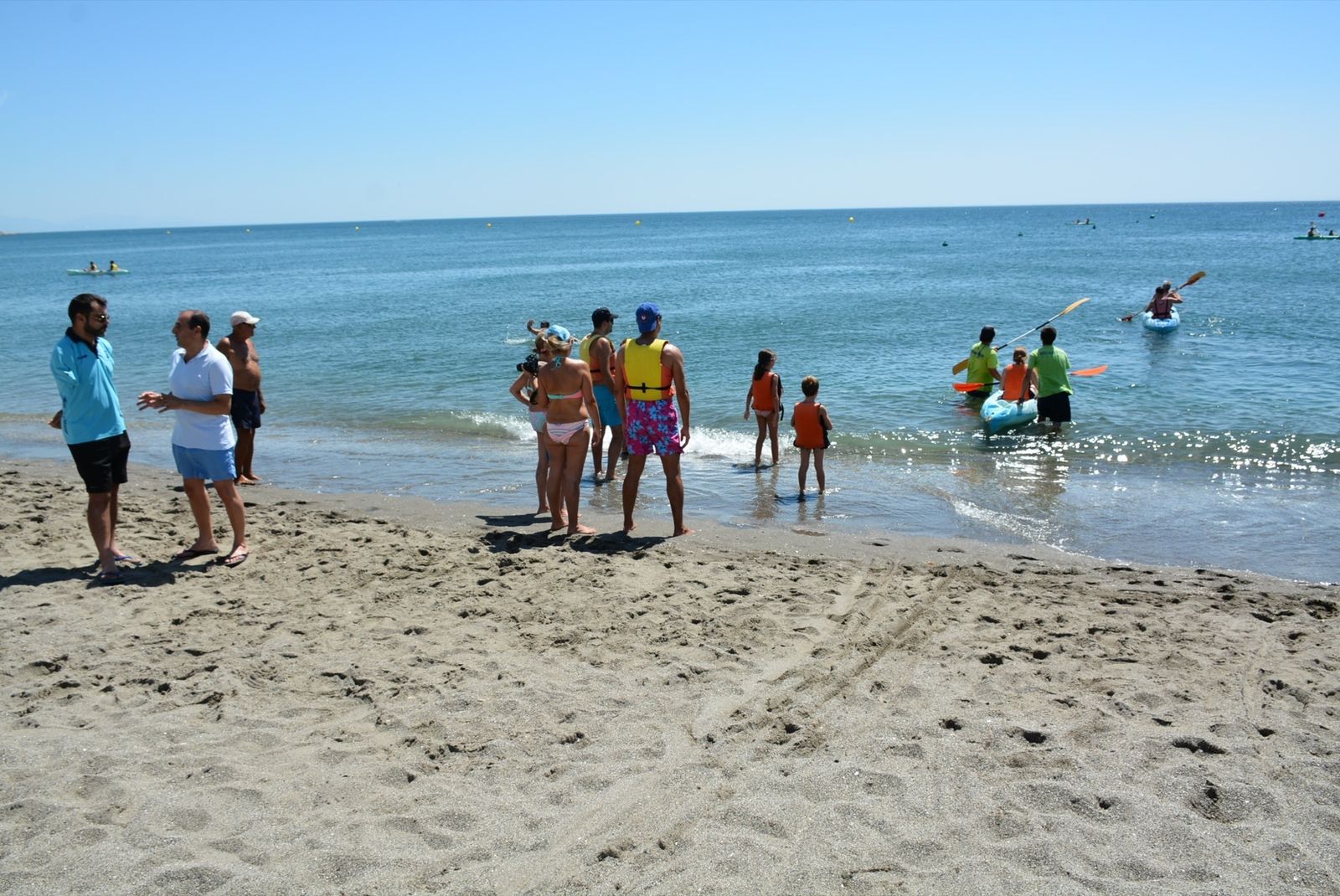 Un grupo de personas observa varios kayak en la playa de Torreguadiaro.