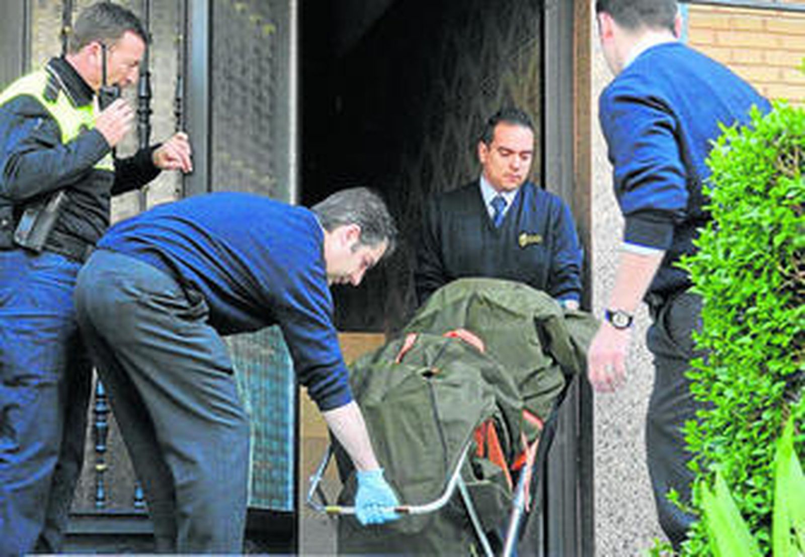 Policías y operarios de los servicios funerarios sacan el cadáver de la mujer de su domicilio.