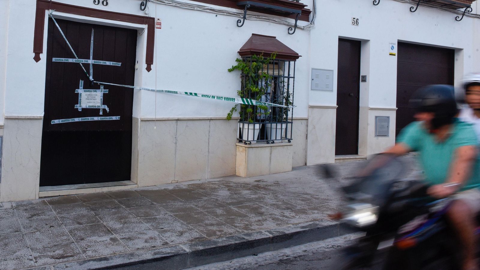 Una moto pasa ante la casa, en cuya puerta se aprecia la suciedad tras la salida de los cuerpos.