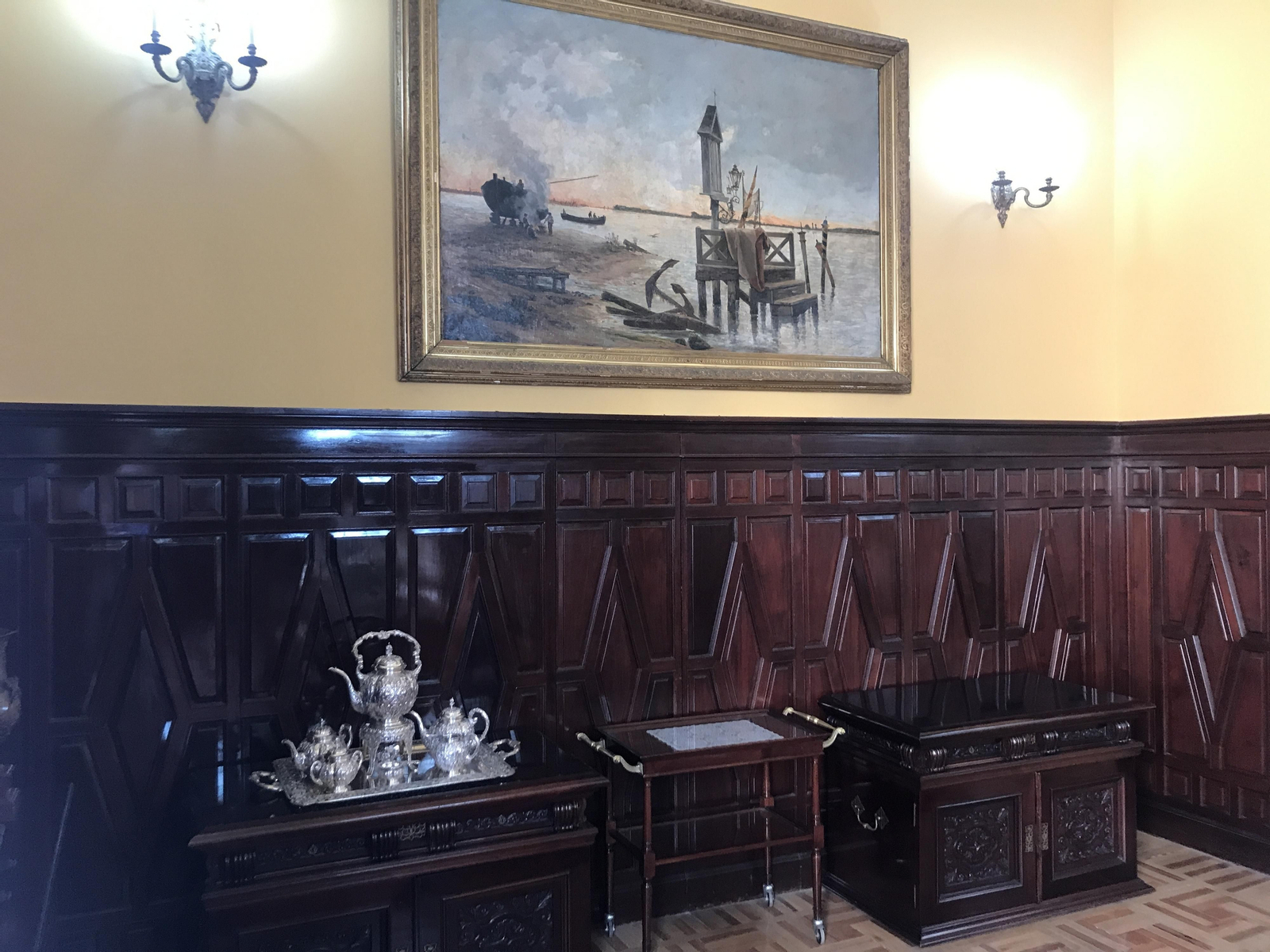 Rincón de sala de estar caracterizado por las maderas, obra pictórica y juego de café de plata.