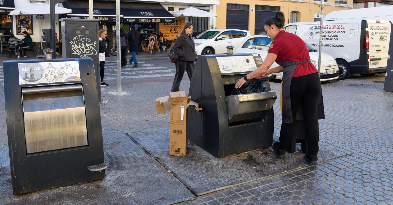Una empleada del sector comercial echa una bolsa al contenedor gris de restos.