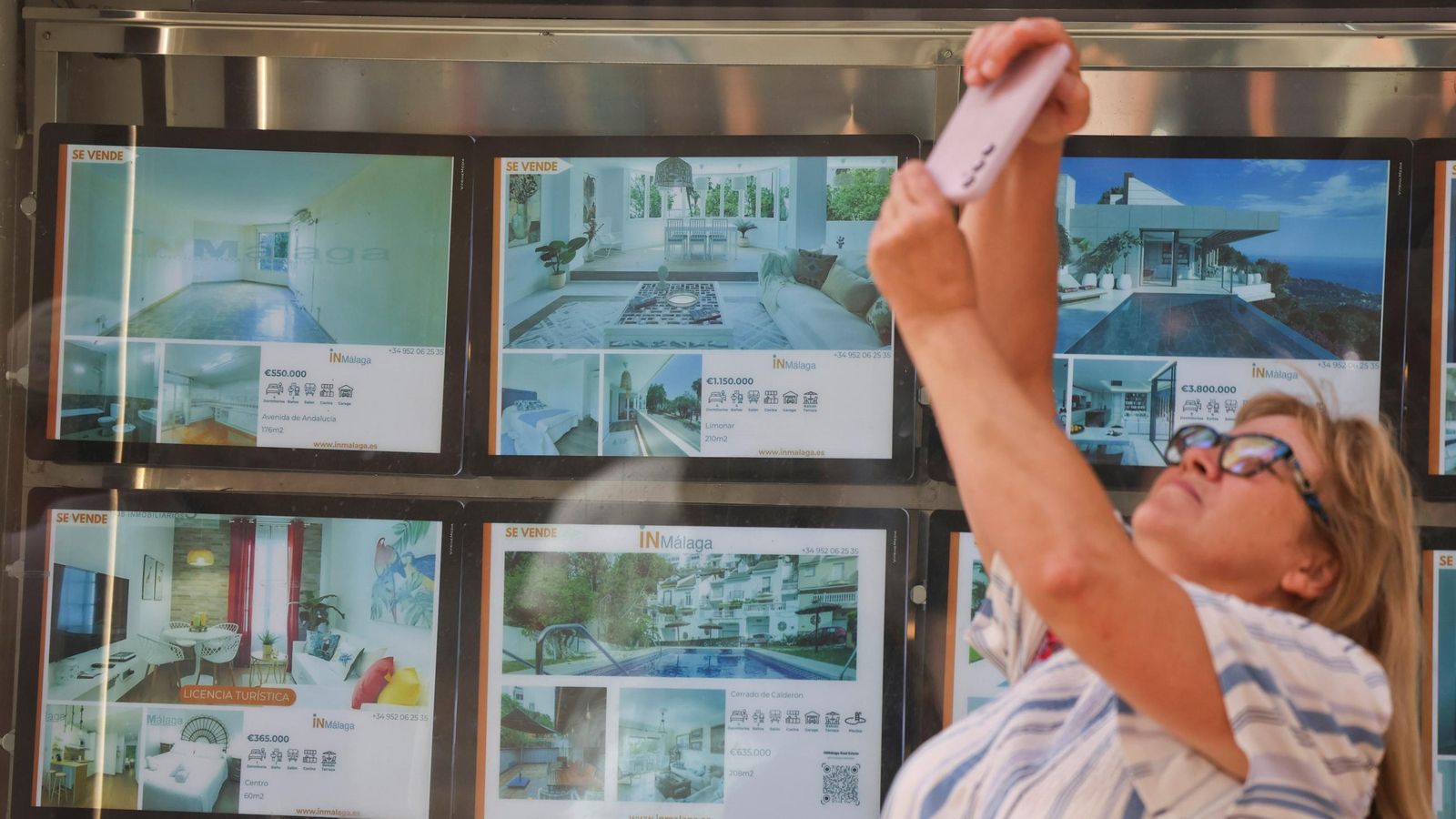 Una mujer utiliza su móvil frente al escaparate de una inmobiliaria