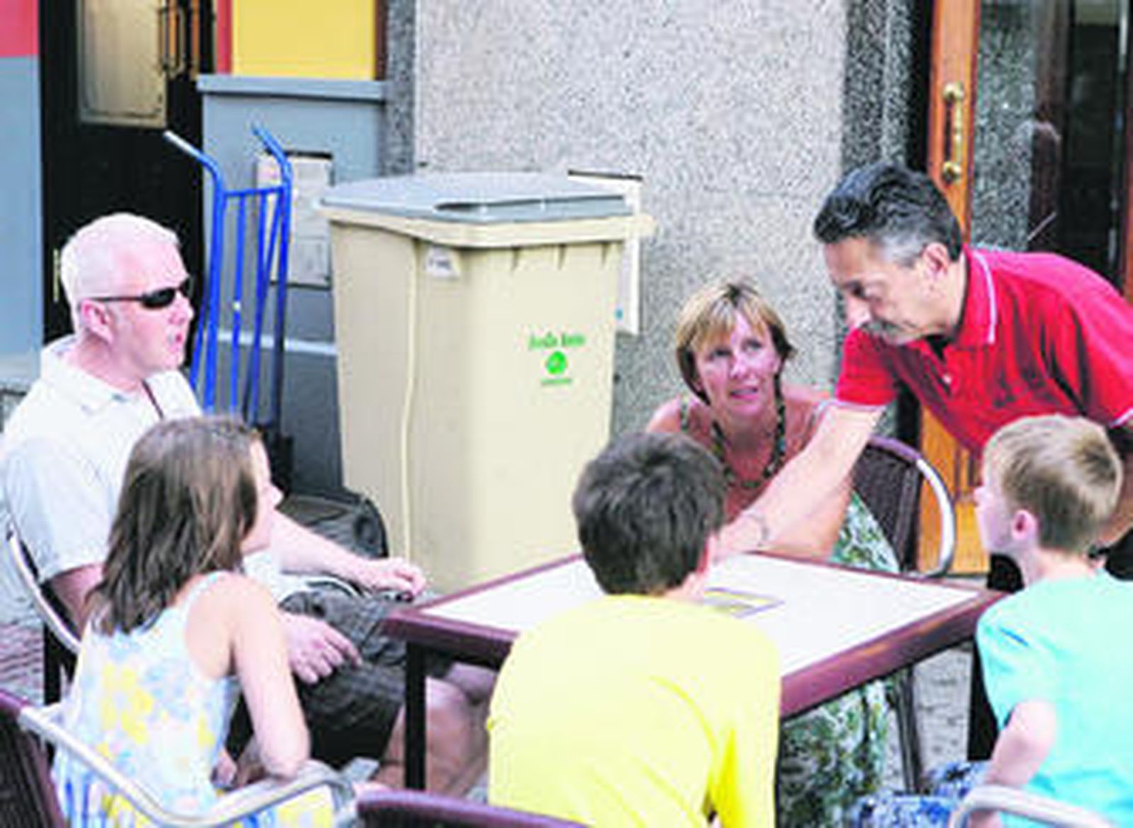 Clientes en el velador de un bar del centro con un contenedor de basuras al fondo.