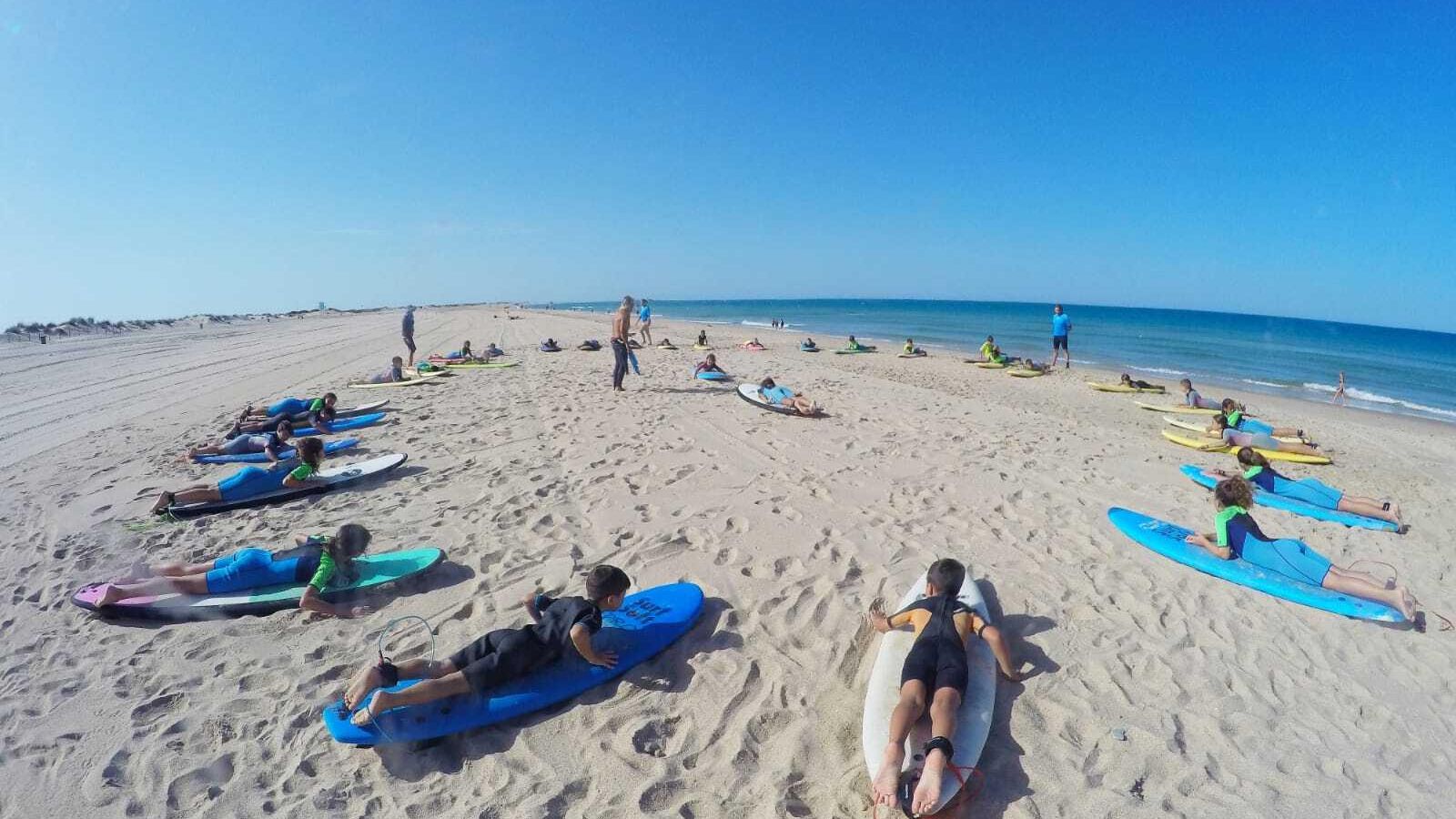 Varios alumnos se preparan en la arena y reciben indicaciones de sus monitores antes de meterse en el mar.