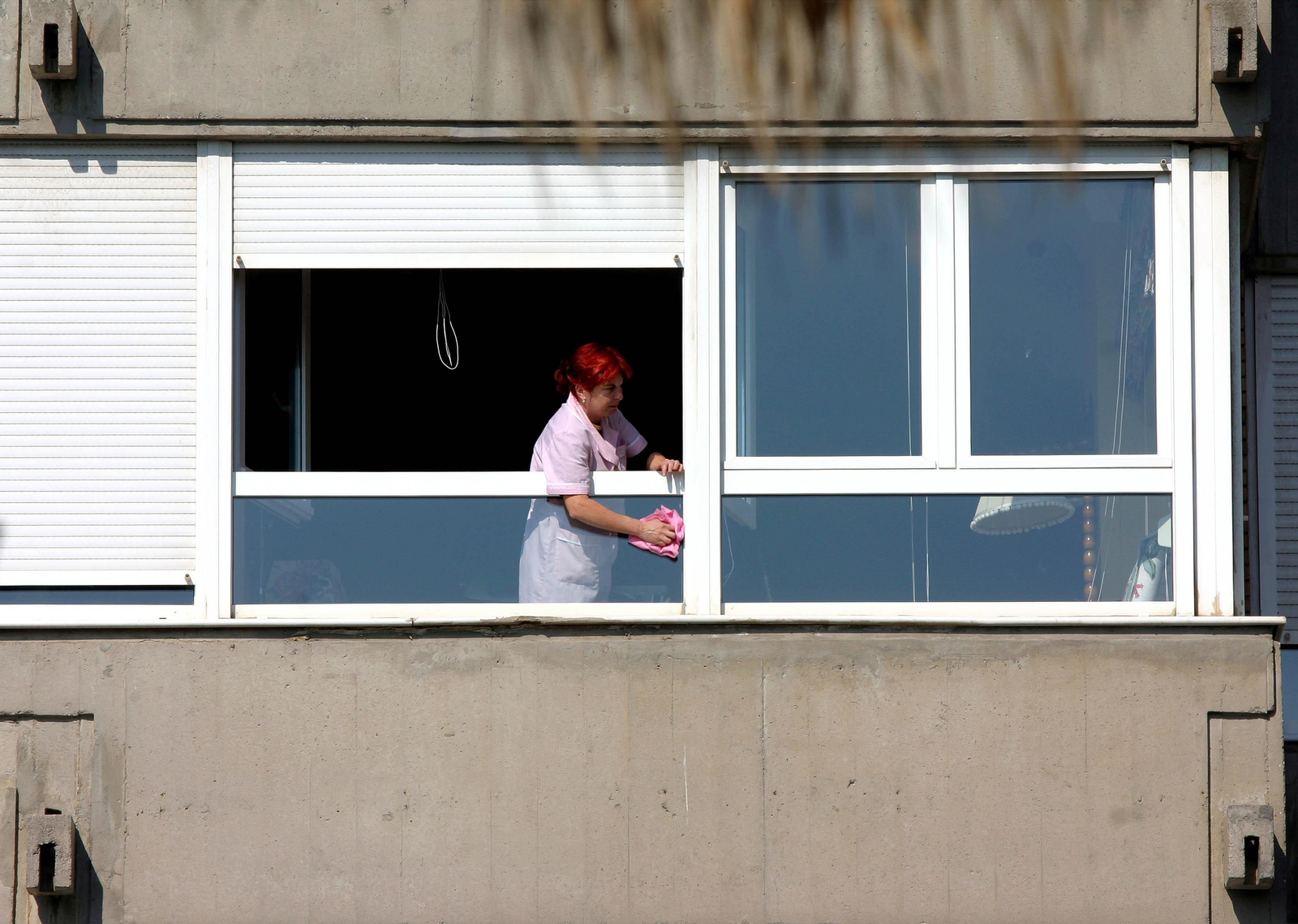 Una empleada del hogar limpia una ventana.