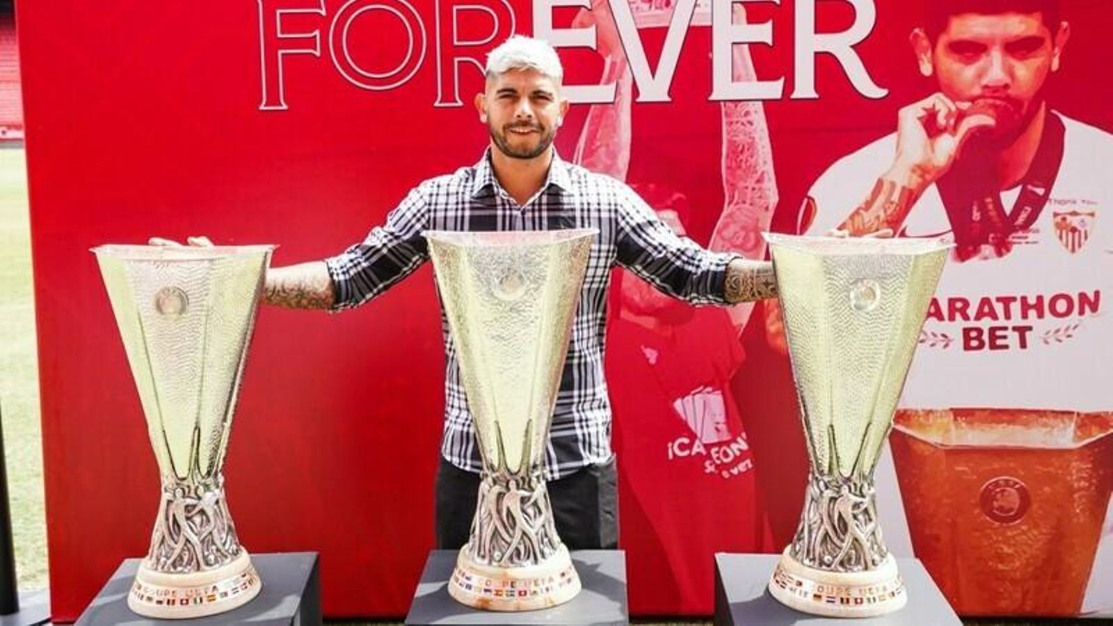 Banega, ante las tres Europa Leagues que ganó, en un montaje que le preparó el Sevilla en el césped.