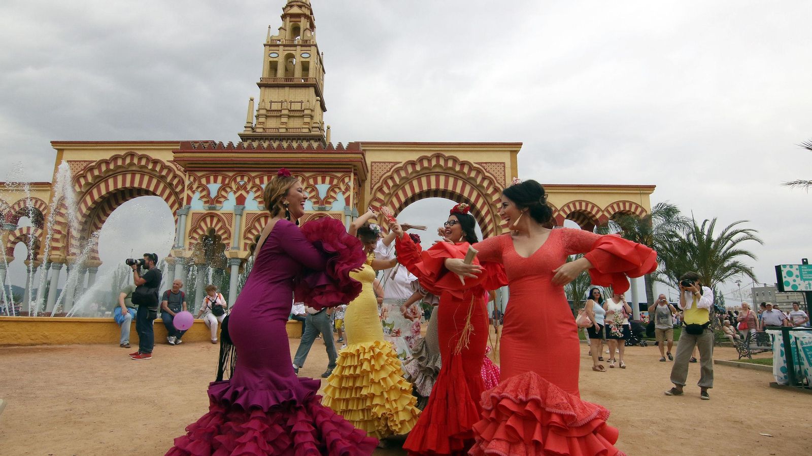 Un grupo de mujeres vestidas de flamenca baila delante de la portada de la Feria. Un grupo de mujeres vestidas de flamenca baila delante de la portada de la Feria.