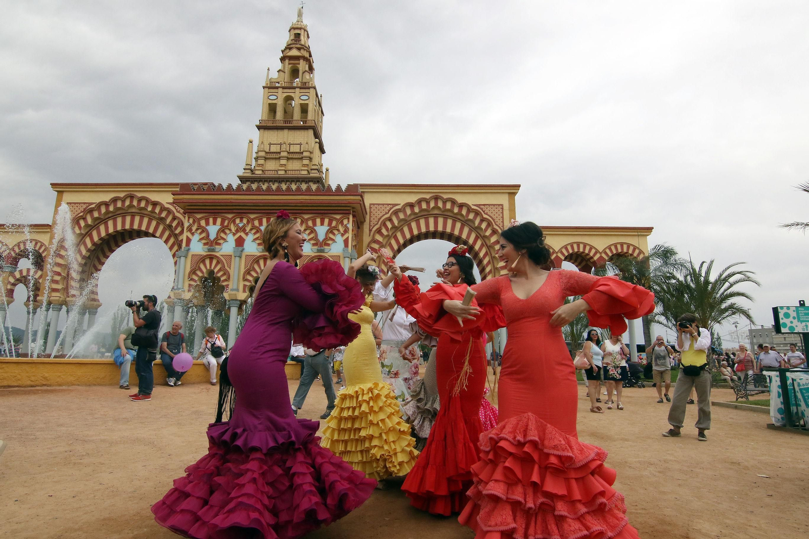 Un grupo de mujeres vestidas de flamenca baila delante de la portada de la Feria.