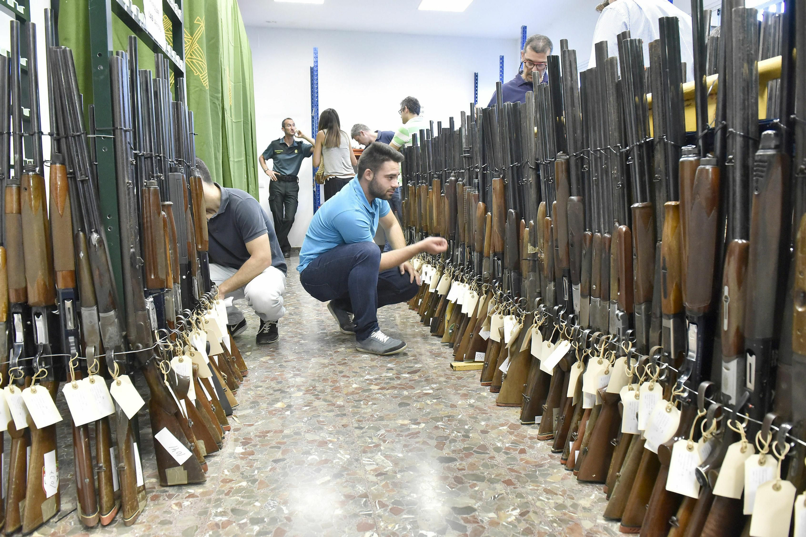 Dos personas miran escopetas en la Intervención de Armas de la Guardia Civil.