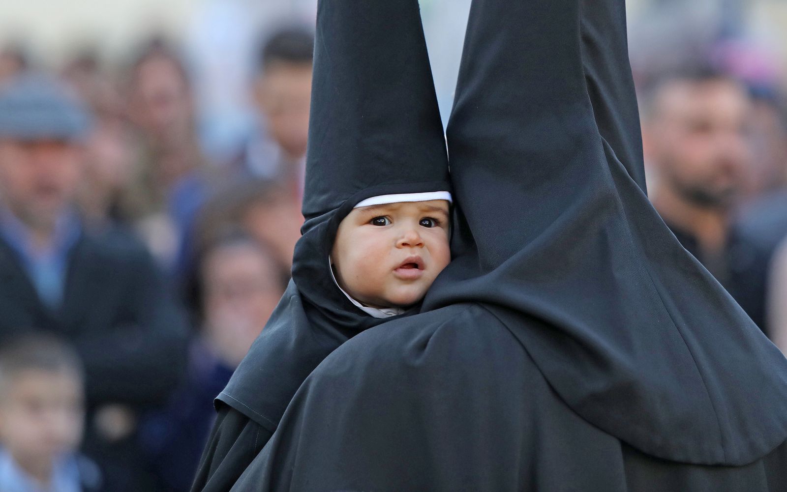Un pequeño nazareno en la salida de la cofradía de la Oración en el Huerto cogido en brazos de un cofrade.