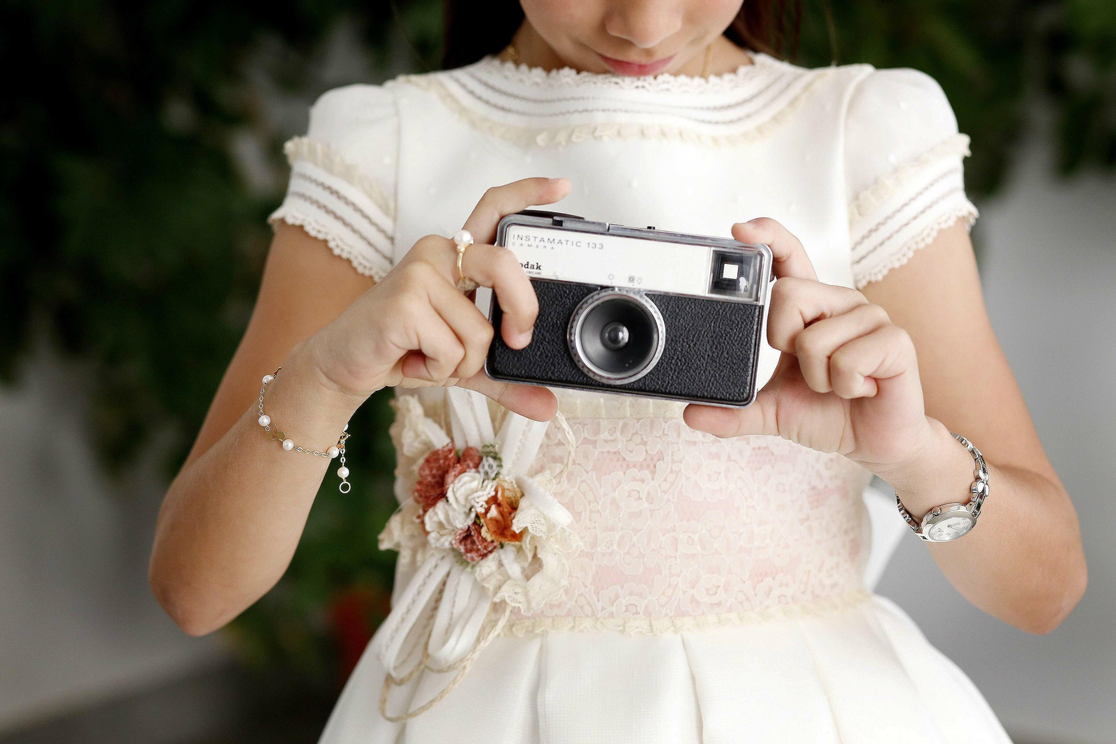 Niña vestida con el traje de la primera comunión y una cámara de fotografías.