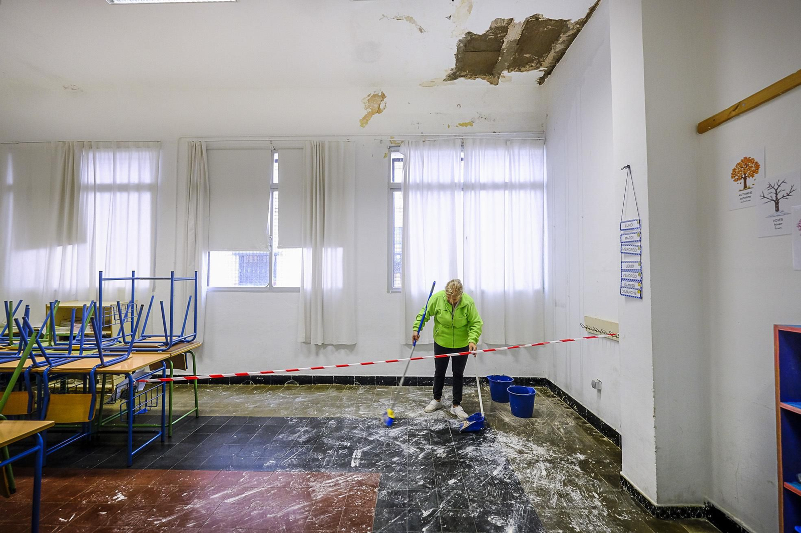 Una limpiadora retira trozos del techo que cayeron en el aula de 5º y detrás, dos cubos recogen el agua de las goteras.