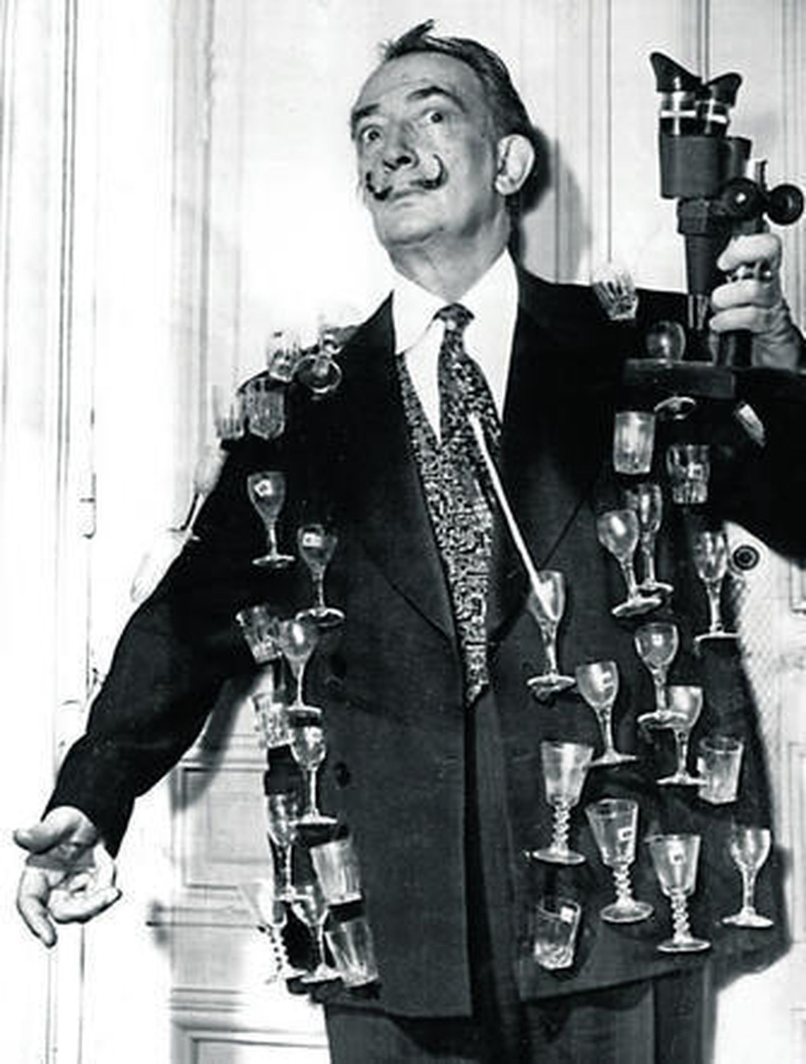 1. Dalí, en París en 1964, con una chaqueta bordada con copas de cristal. 2. Un cartel que recogía la exposición 'Dalí. Cultura de masas' que se vio en 2004 en el Caixaforum de Barcelona y en el Reina Sofía de Madrid. 3. 'La persistencia de la memoria', una de sus obras más emblemáticas. 4. Con su mujer, Gala.