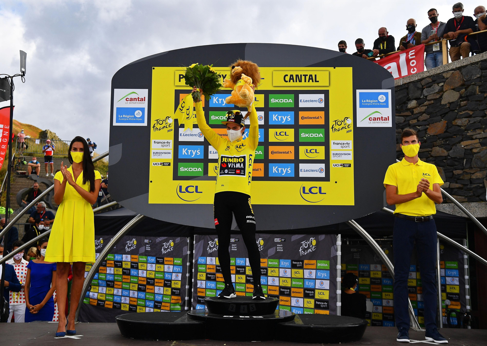 Una pareja mixta entrega el maillot amarillo y los regalos al líder del Tour Roglic
