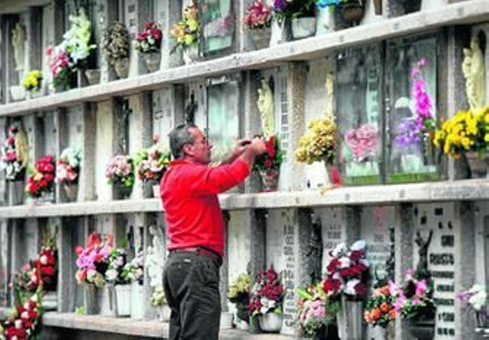 Un hombre pone flores en un nicho del cementerio San Gabriel.