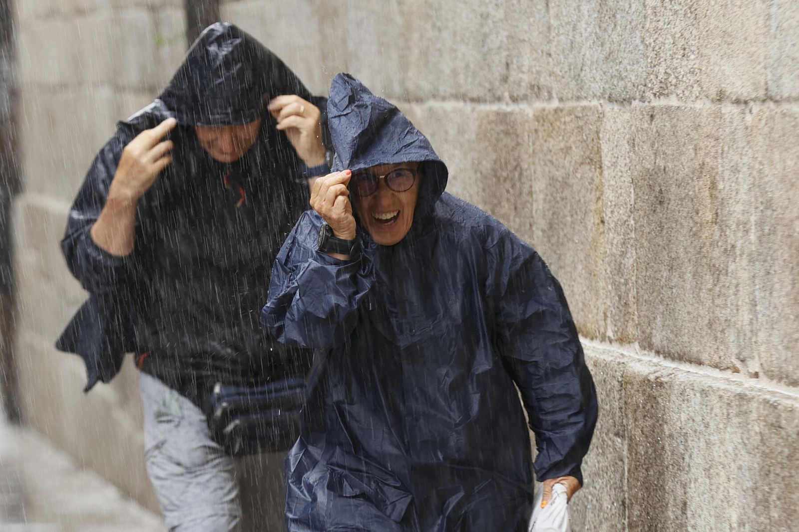 Turistas corren cubiertos con un chubasquero durante una tormenta en Sevilla.
