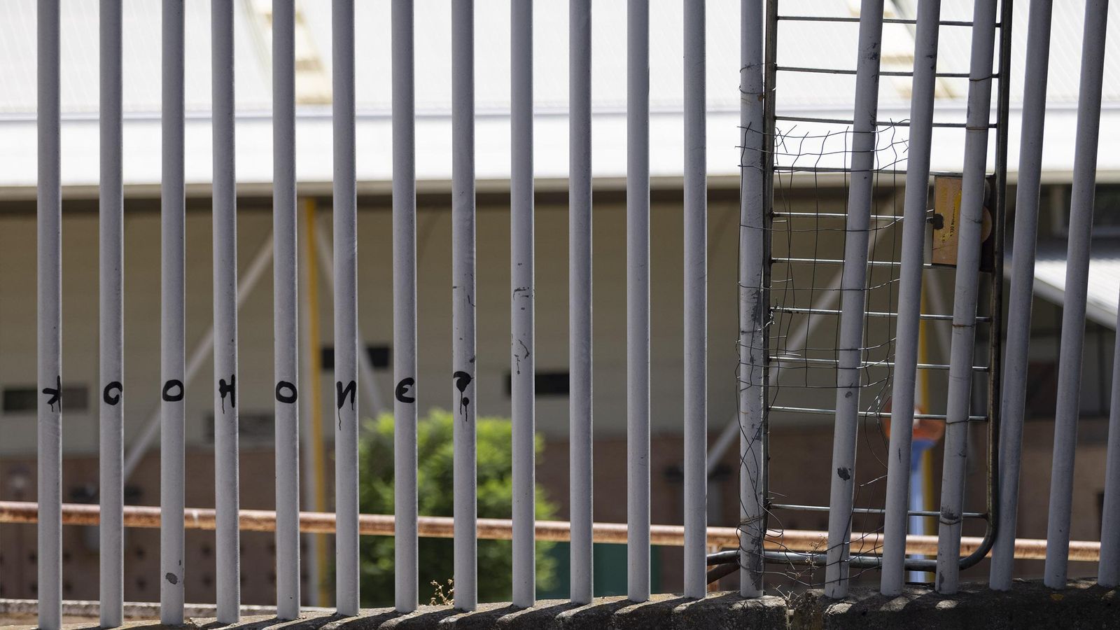 Una valla metálica de tráfico colgada en un hueco del vallado por donde se accede a la caseta ocupada.