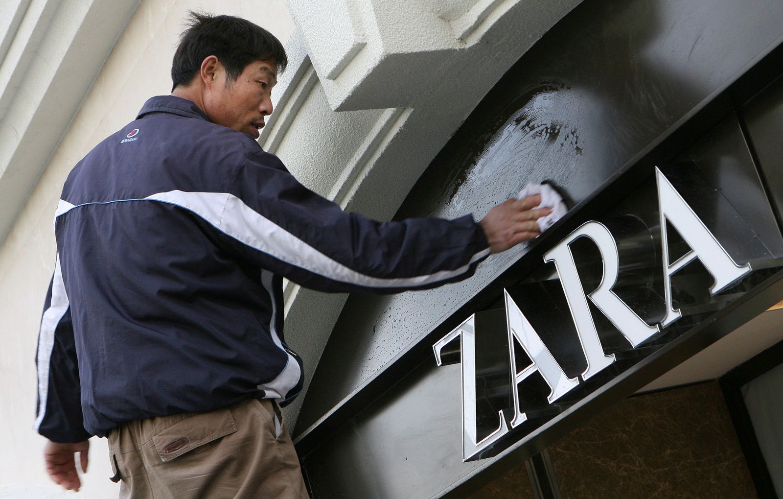 Un trabajador limpia el cartel de Zara en una tienda de Shanghai.